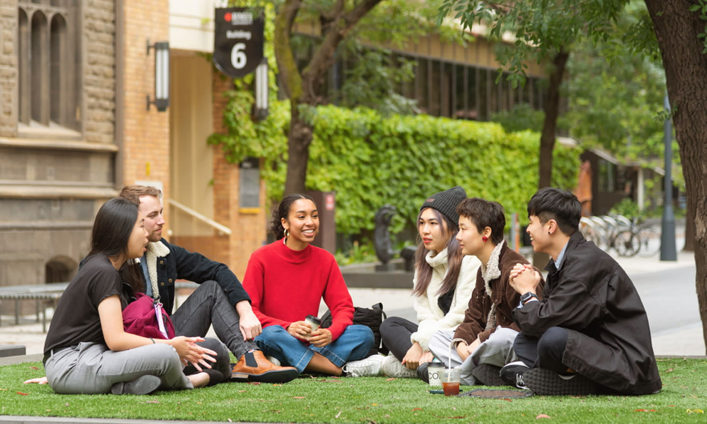 Six students sit on a patch of lawn talking
