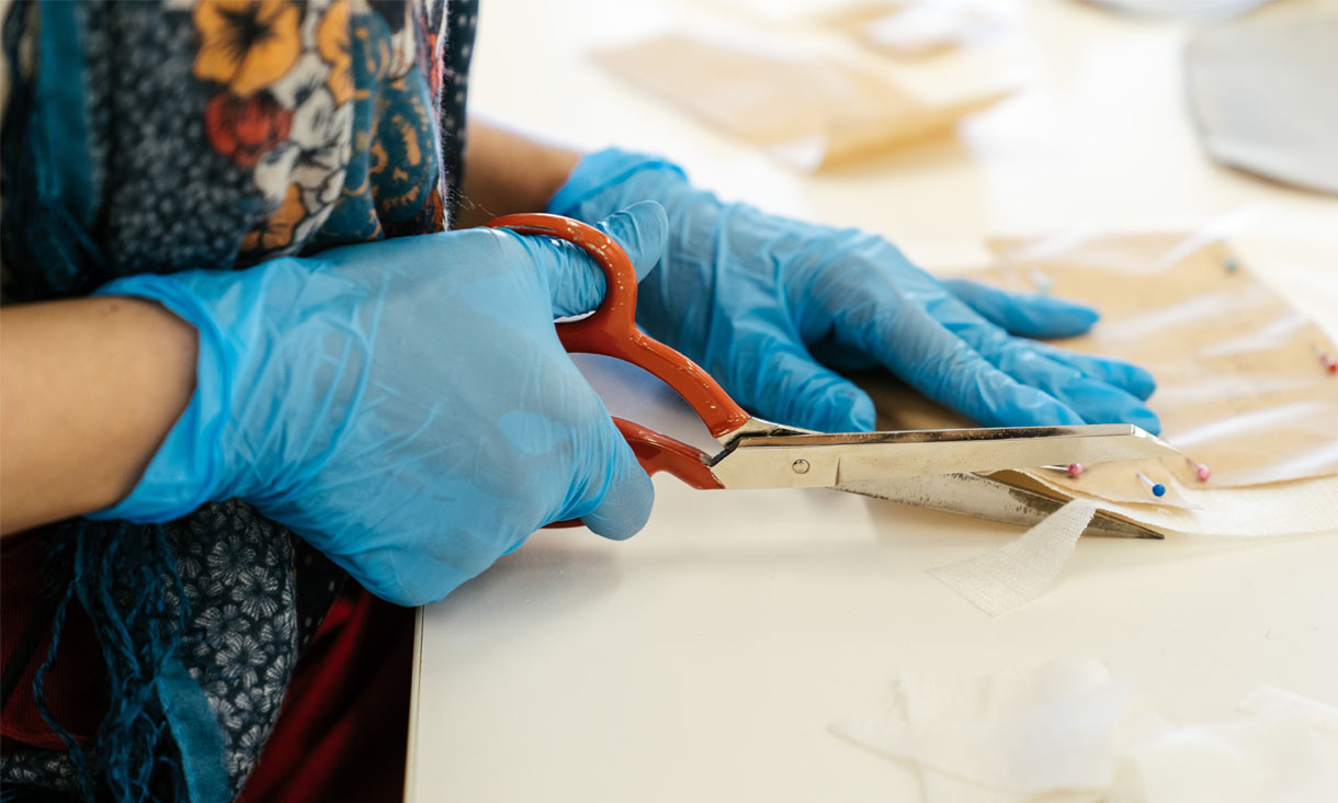 A person wearing blue latex gloves cuts fabric following a clothing pattern.