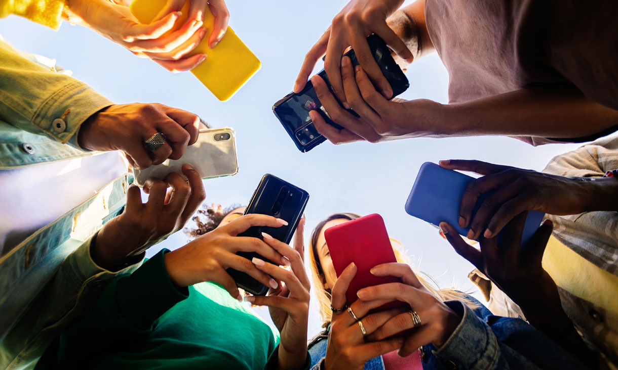 A group of people wearing colourful clothing use their phones in a circle. Their phone cases are also very colourful. Credit: Xavier Lorenzo, Adobe Stock