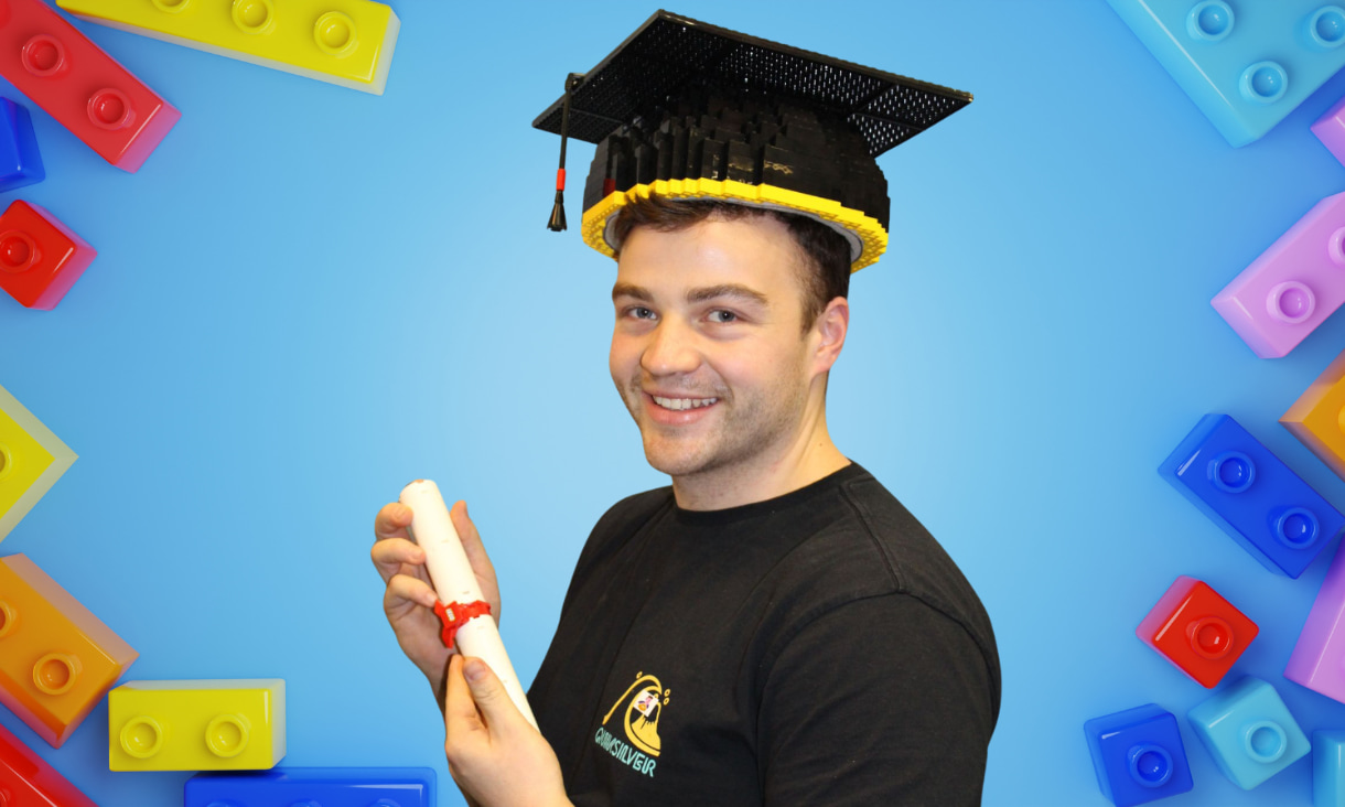Nick Johnson wearing a graduation mortar board and holding a scroll with a blue background and Lego blocks